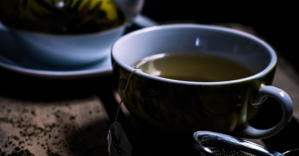 A cozy dark wooden setup with green tea in a teacup, teapot, and strainer.